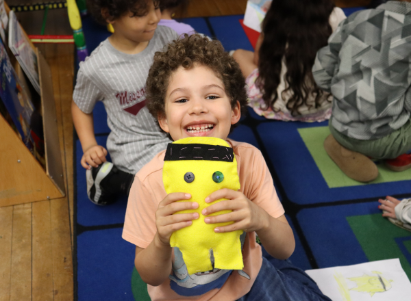  Student smiles while holding their stuffed animal made by Reed Academy students